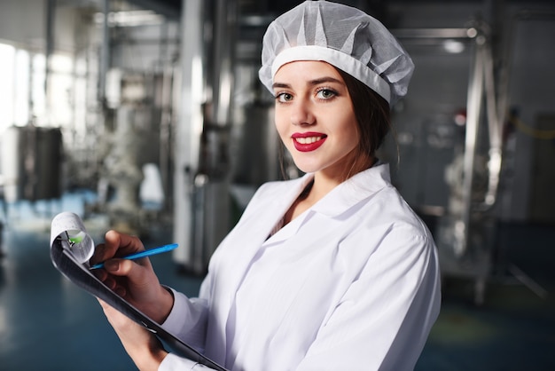 Chica científica o trabajadora en uniforme blanco hace notas en papel.