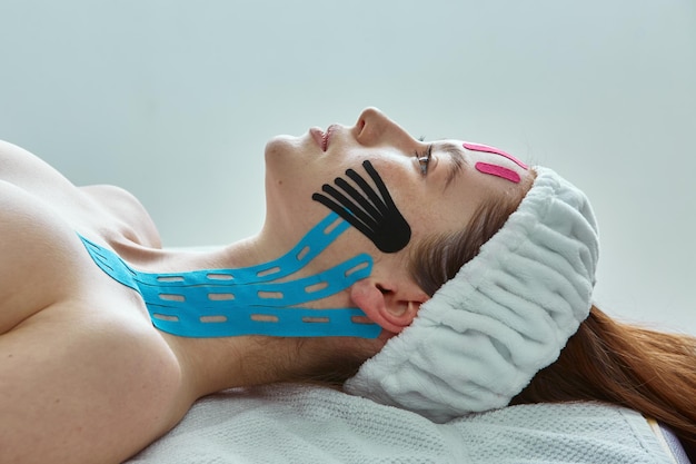 Chica con cintas de estiramiento facial en las mejillas del cuello acostada durante el procedimiento de tratamiento rejuvenecedor kinesio tape