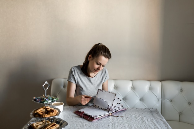 Foto chica en la cocina se sienta a la mesa hojea un libro.