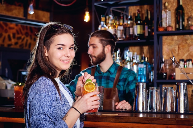 Una chica con cóctel sonríe detrás del mostrador en el bar