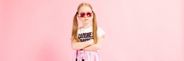 Chica con colas rojas un rosa. Una chica encantadora con ropa deportiva brillante y lentes rosas cruzó los brazos sobre el pecho.