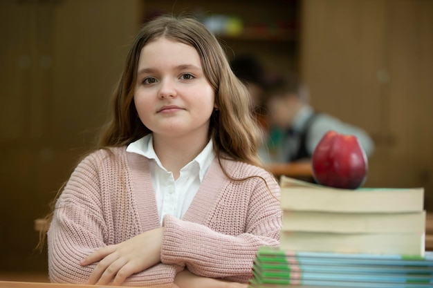 Chica colegiala en el escritorio Chica en el aula con libros y una manzana