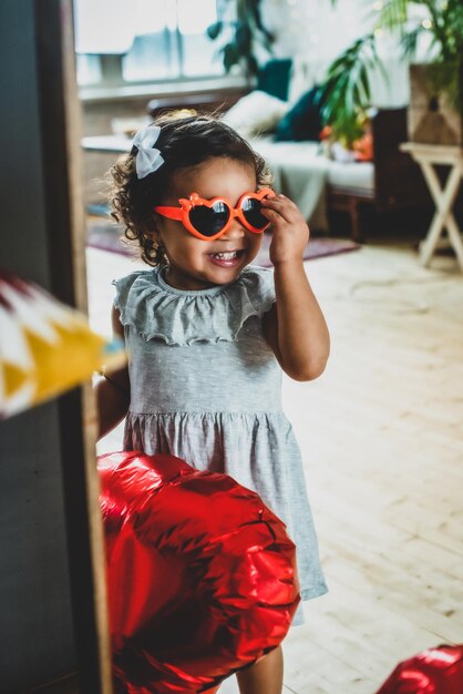 Chica con color de piel negro oscuro celebra el día de san valentín con globos y vasos de lámina roja en forma de corazón