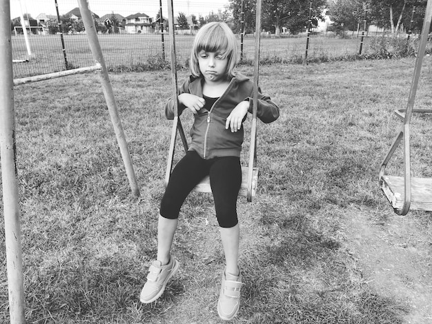 Chica en un columpio Fotografía retro monocromática Un niño con uniforme deportivo se balancea En el fondo está el estadio Tristeza en la cara La emoción de la frustración y el sentimiento de soledad