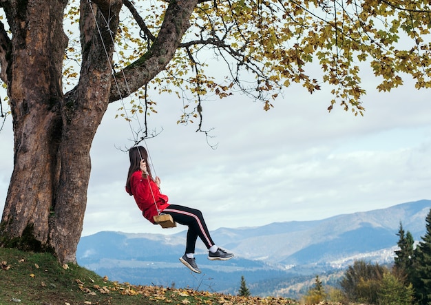 Chica en un columpio de vacaciones con vistas a las montañas y bosques.