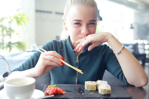 Chica come sushi y rollos en un restaurante / cocina oriental, comida japonesa, modelo joven en un restaurante