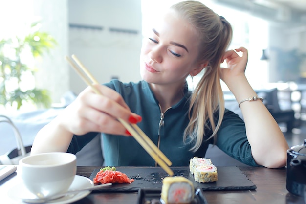 Chica come sushi y rollos en un restaurante / cocina oriental, comida japonesa, modelo joven en un restaurante