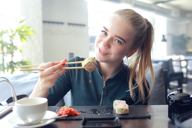 Chica come sushi y rollos en un restaurante / cocina oriental, comida japonesa, modelo joven en un restaurante