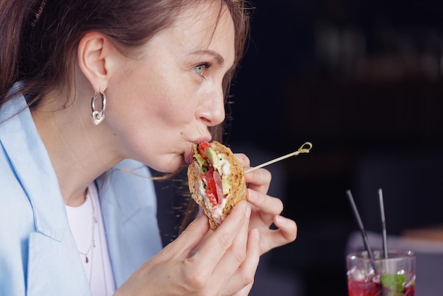 Chica comiendo un delicioso sándwich de cerca en un café moderno