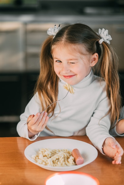 Foto chica comiendo pasta con salchicha en la cocina con una chaqueta de rayas