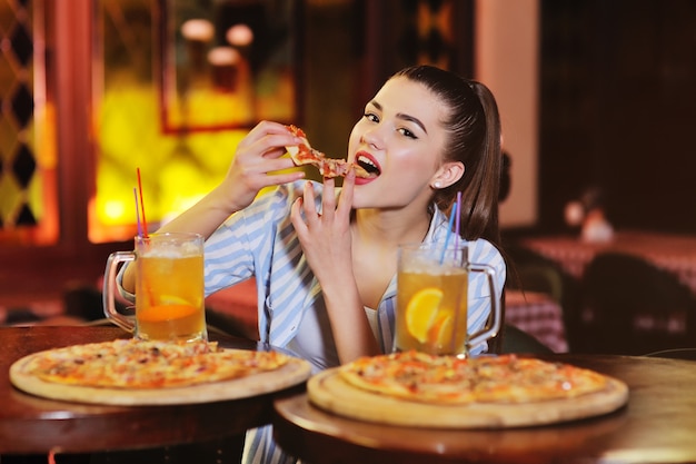 chica comiendo pizza y bebiendo cerveza o un cóctel de cítricos de cerveza en el fondo de un bar o pizzería.