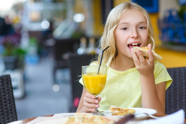 Chica comiendo pizza y bebiendo jugo al aire libre