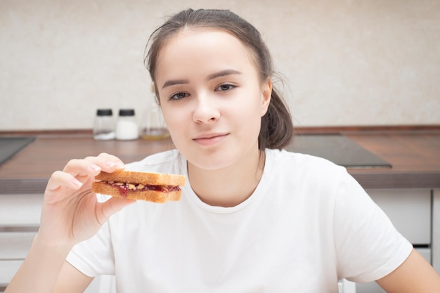 Chica comiendo un sándwich por la mañana en la cocina en la mesa.