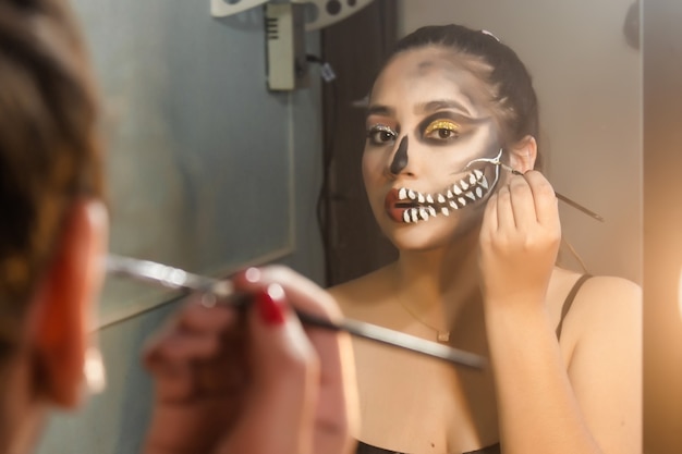 Chica concentrándose en hacer una calavera artística para Halloween en su habitación.