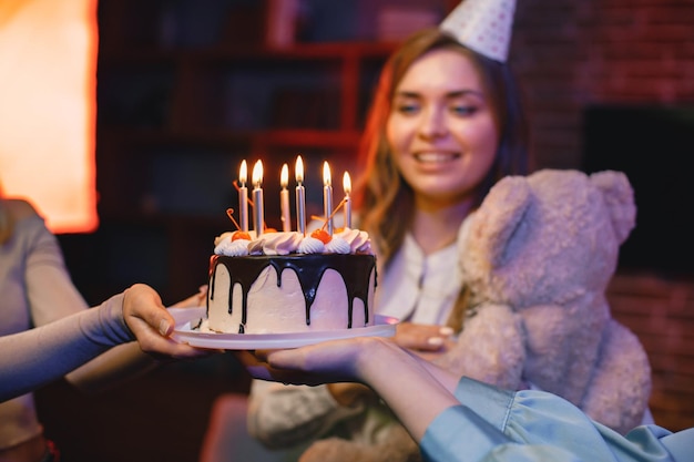 Chica en cono de fiesta de pie cerca de un plato con un pastel y celebrando un cumpleaños