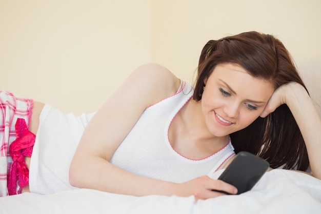 Chica contenta usando un teléfono móvil acostado en una cama