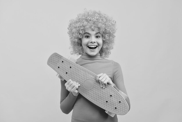 Chica cool feliz con cabello naranja en sonrisa de poloneck rosa con monopatín de pennyboard