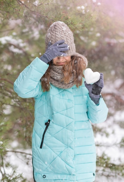 Chica con un corazón de nieve en sus manos en la naturaleza