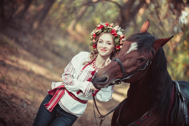 Chica en una corona y camisa bordada con un caballo en el bosque