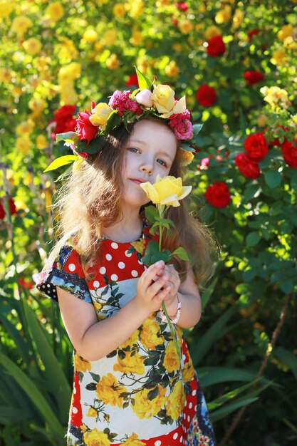 Chica en una corona de flores en el jardín con una rosa amarilla