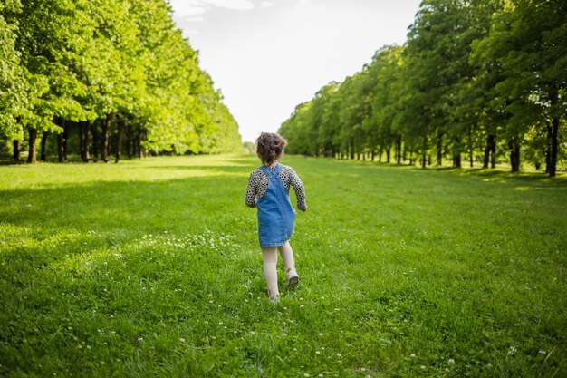 Chica corriendo en un vestido de mezclilla en un prado de verano con tilos.