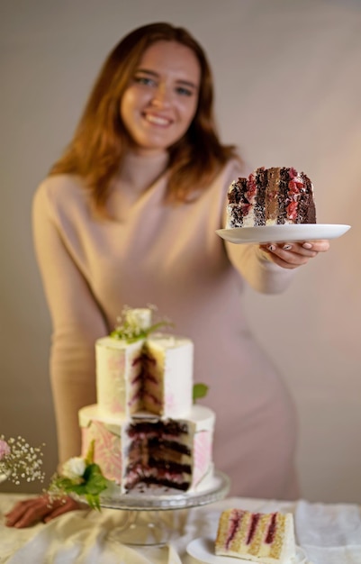 La chica corta y sirve un trozo de pastel de boda festivo de dos niveles decorado con flores frescas sobre un fondo gris