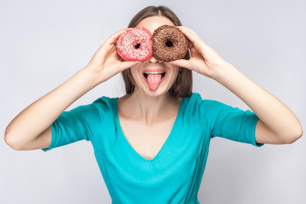 Chica cubriéndose los ojos con rosquillas de chocolate y rosa mirando a través de donas