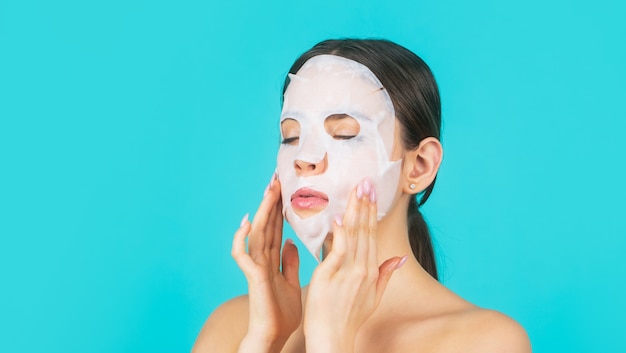 Chica cuidando el cutis de la piel. Concepto de belleza y cuidado de la piel. Mascarilla hidratante. Mujer aplicando mascarilla en el rostro, sobre fondo azul. Bella mujer con máscara.