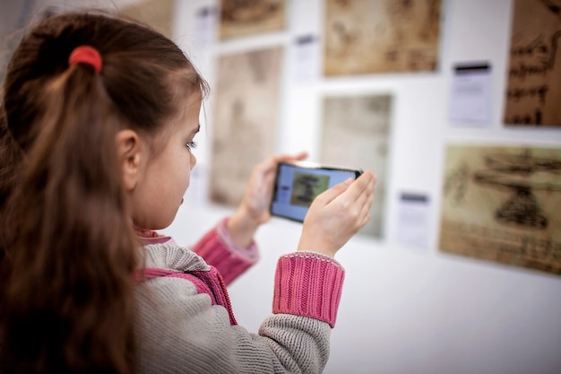 Chica curiosa explorando una exposición de arte contemporáneo con aplicación móvil de realidad aumentada