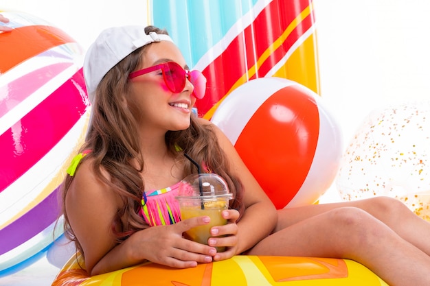 Chica curtida bebe un batido en la pared de colchones y pelotas inflables