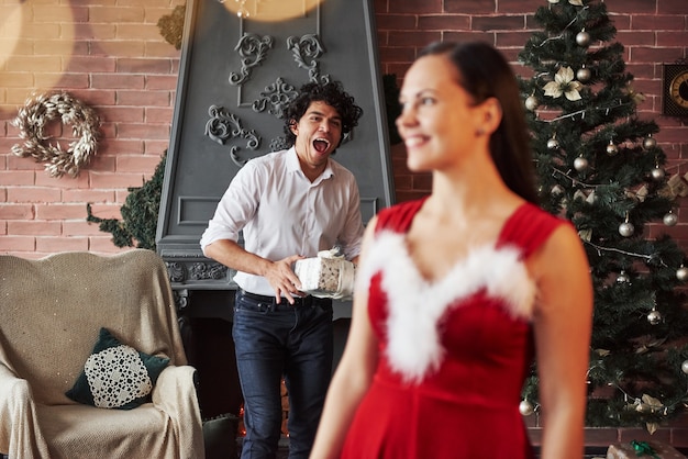 La chica se va a dar la vuelta y verá al chico parado con el presente detrás. La mujer con vestido rojo ahora recibirá un regalo de Navidad de su novio.