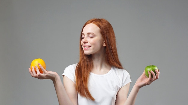 Chica decidiendo entre dos frutas, una manzana y una naranja.