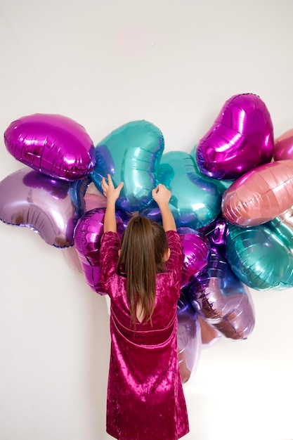 Chica decora la pared de la habitación con globos de colores vivos para el Día de San Valentín