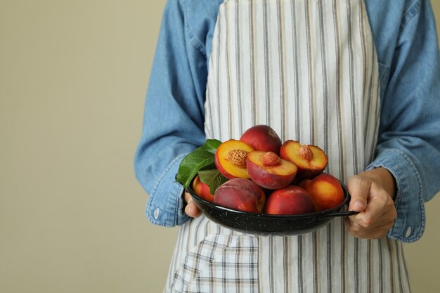 Chica en delantal tiene tazón con frutos maduros de melocotón