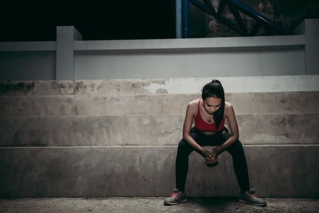 Chica delgada asiática sentada en standshe cansada del ejercicio en la escena nocturna