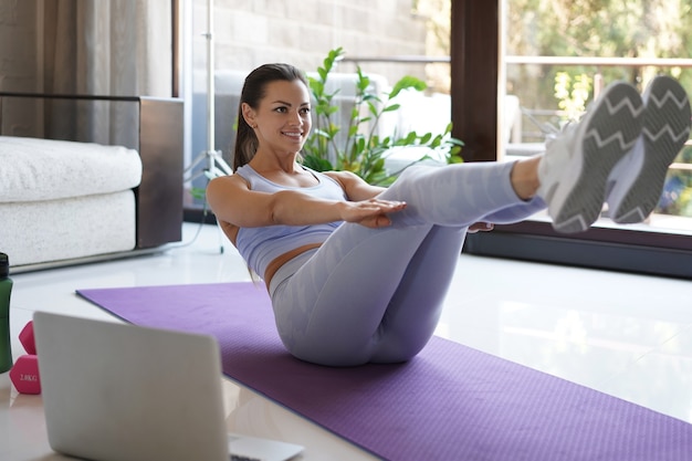 Chica delgada atractiva en ropa deportiva está haciendo ejercicio de abs en el suelo en casa. Estilo de vida saludable.