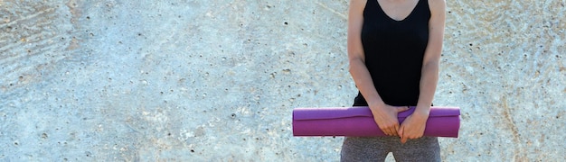 Una chica delgada deportiva con leggings y un top está de pie con una colchoneta de entrenamiento, descansando entre ejercicios.