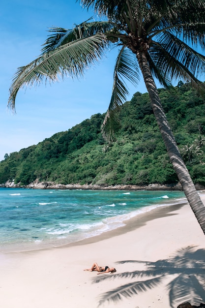 Foto una chica delgada está descansando bajo una palmera en una playa tropical. clima cálido
