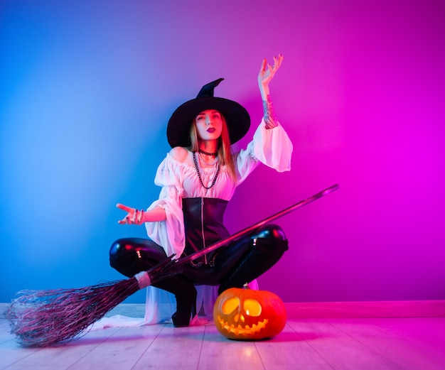 La chica delgada con un disfraz de bruja para Halloween con una escoba y una calabaza