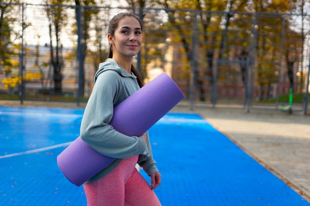 Chica delgada con una estera de yoga en las manos