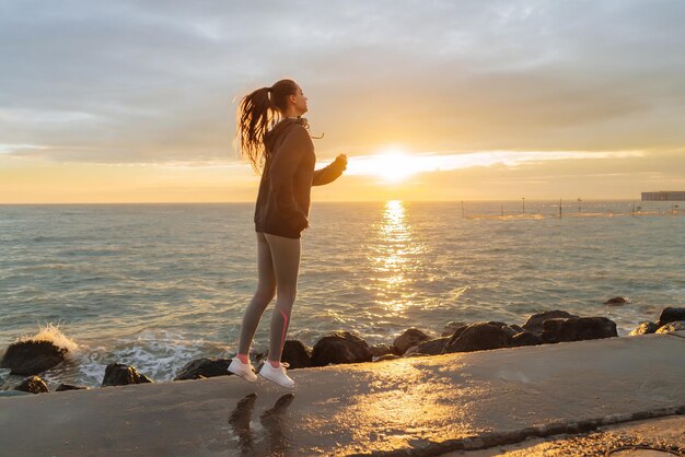 Chica delgada y rápida haciendo deportes en el mar corriendo al atardecer