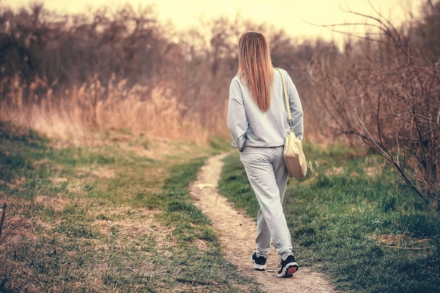 Una chica delgada con ropa informal camina sola por el camino del parque