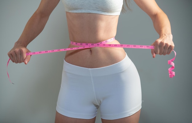 Chica delgada sosteniendo un centímetro alrededor de la línea de la cintura. Mujer joven delgada midiendo su cintura con una cinta métrica, pérdida de peso.