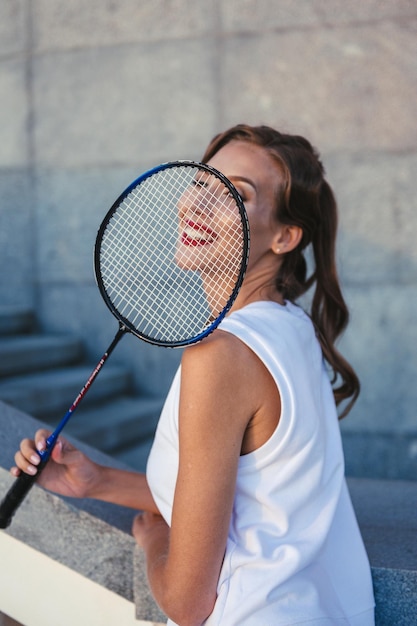 Chica delgada en traje deportivo blanco con raqueta de bádminton en la mano