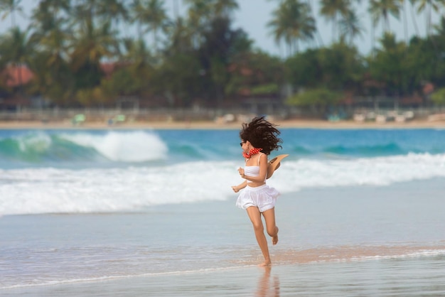 Una chica delgada vestida de blanco corre por la playa contra el fondo del mar