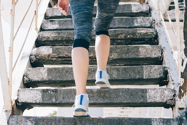 Chica delgada en zapatillas y ropa deportiva subir escaleras, primer plano