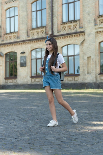 Chica denim feliz con mochila caminando al aire libre