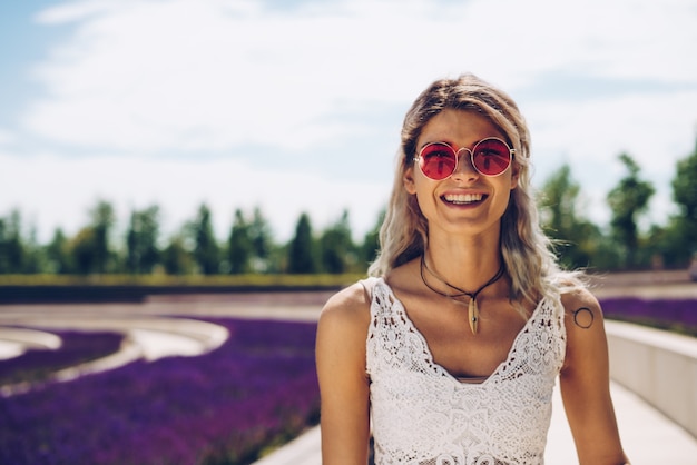 Chica de deportes en gafas de color rosa sonríe con alegría en el contexto de la flor de salvia