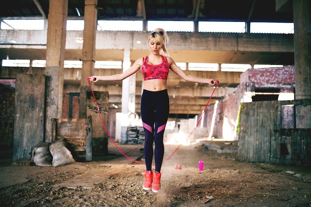 Chica deportiva atractiva está haciendo ejercicios con saltar la cuerda en lugar de abandono.