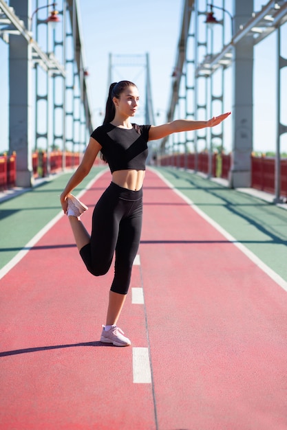 Chica deportiva bastante bronceada que estira las piernas antes de correr. Espacio para texto